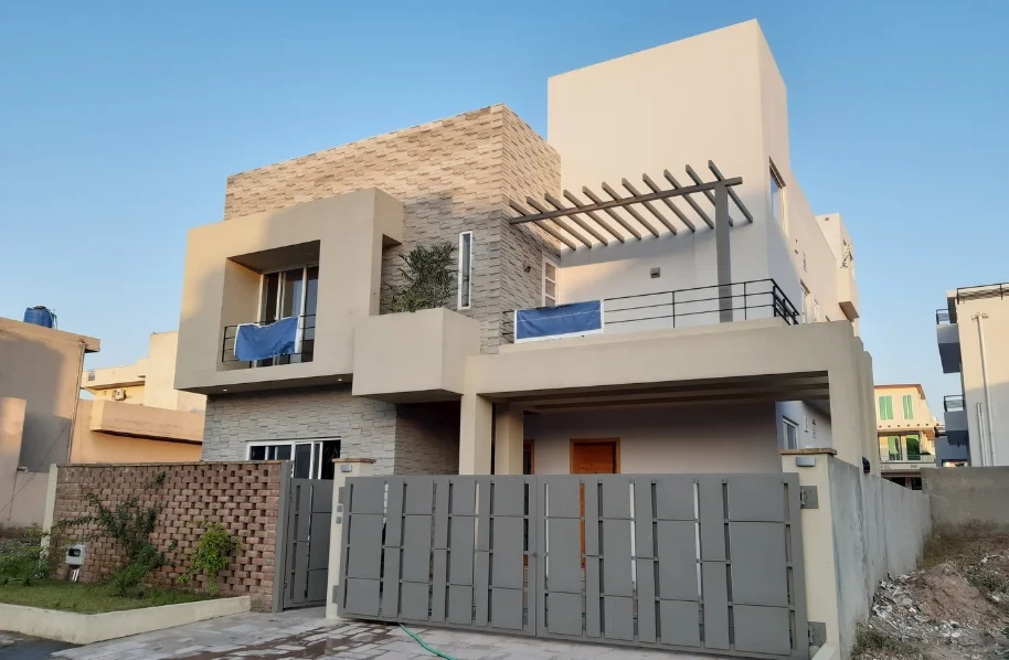 Daylight exterior view of a completed modern house facade with flat roof lines and smooth grey stucco finish in Islamabad.