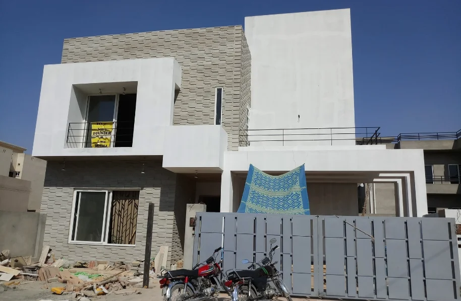 View of a two-story residential structure under construction with concrete frame and block infill, visible on a sunny day.