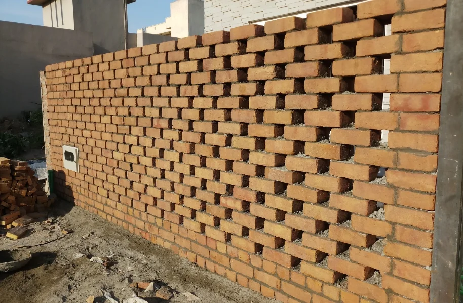 Construction worker installing red bricks in a perforated Jali pattern on a boundary wall.