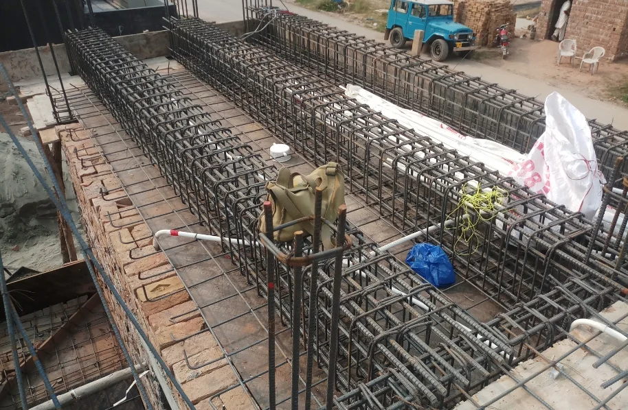 Workers are shown laying and tying steel reinforcement bars (rebar) on the ground before the concrete pour for a floor slab.