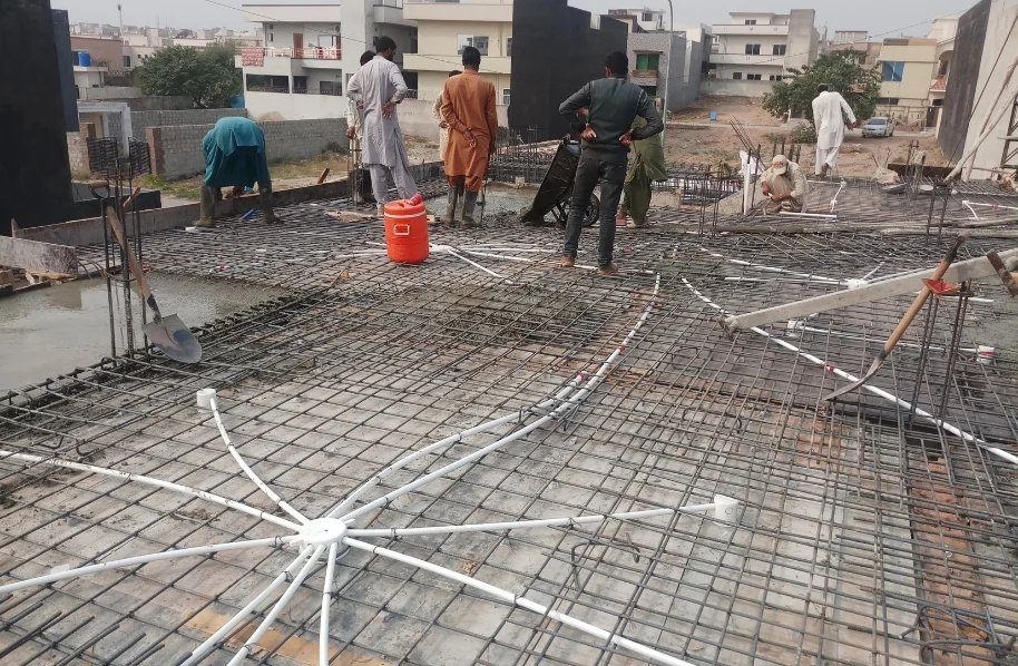 Wide shot of a construction site showing a dense grid of steel rebar laid out for a large concrete ground floor slab.