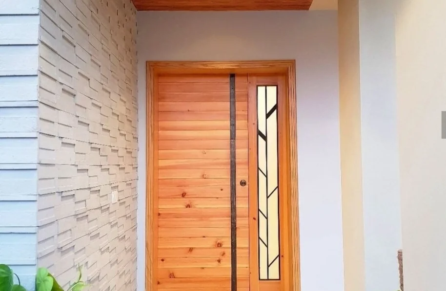 Close-up of a solid wood main entrance door with vertical grain and frosted glass inserts, installed in a light brick wall.