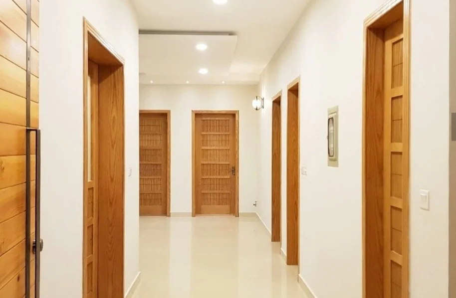 View down a light-colored interior hallway with recessed lighting and two identical wooden doors with dark hardware.