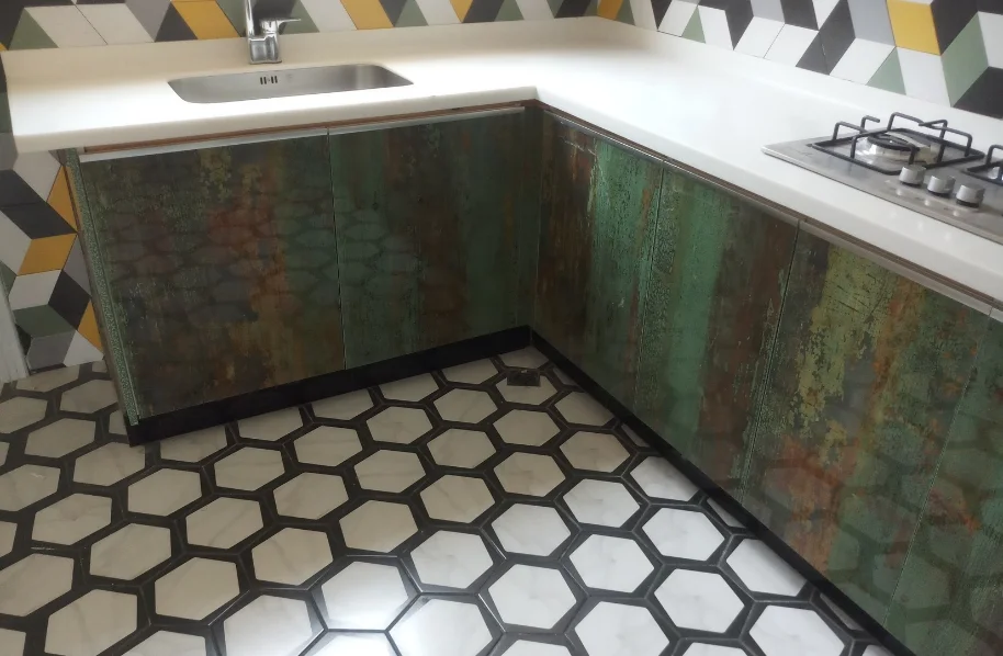 Close-up of a kitchen corner showing a unique oxidized metal-look countertop finish and white hexagonal floor tiles.