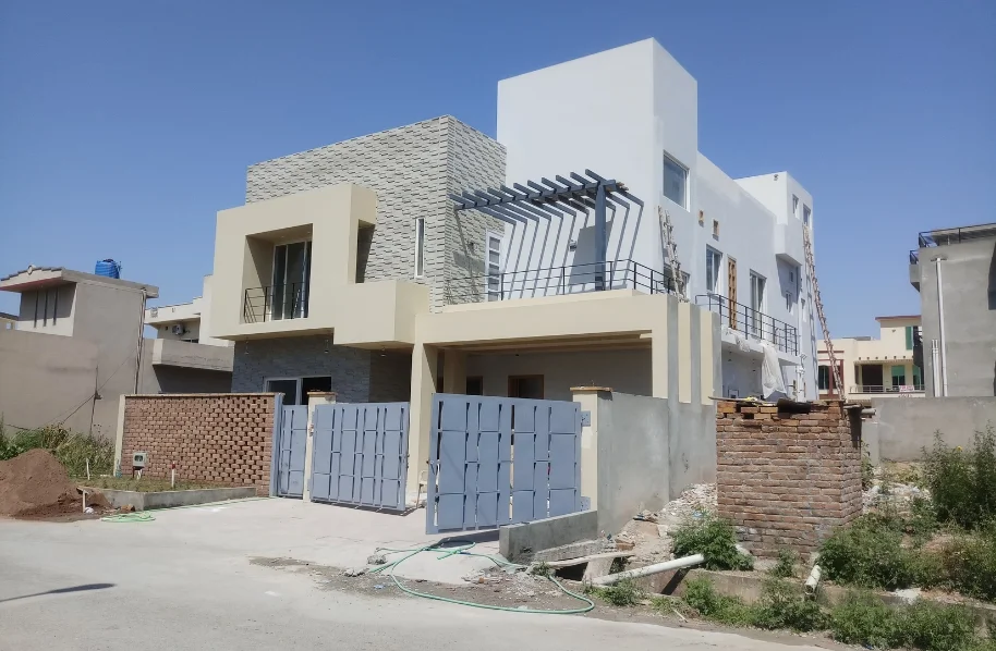 View of a house under construction, featuring exposed blockwork, some blue waterproofing/sheathing, and an incomplete facade.